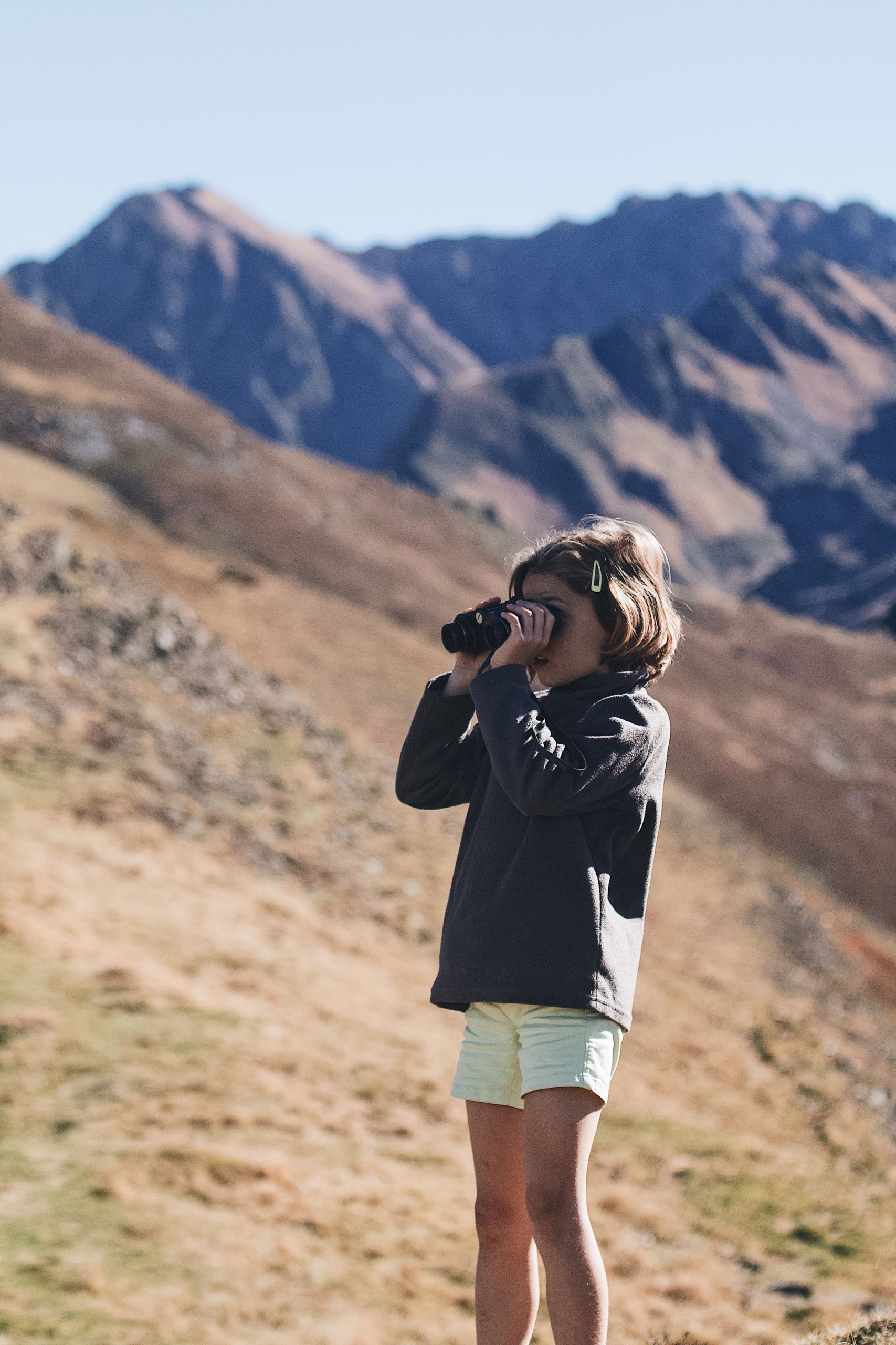 A child explores the mountain scenery with binoculars, embodying adventure and curiosity.