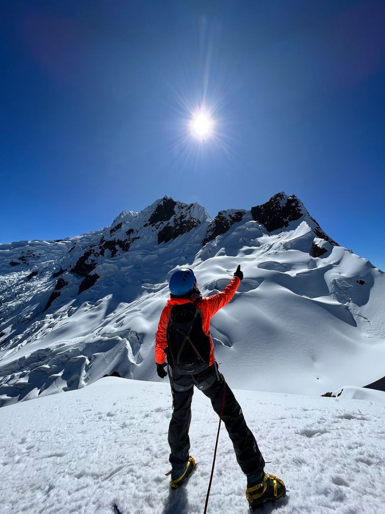 A climber gestures towards the sun atop a snowy peak in the Andes, capturing the spirit of adventure and exploration.