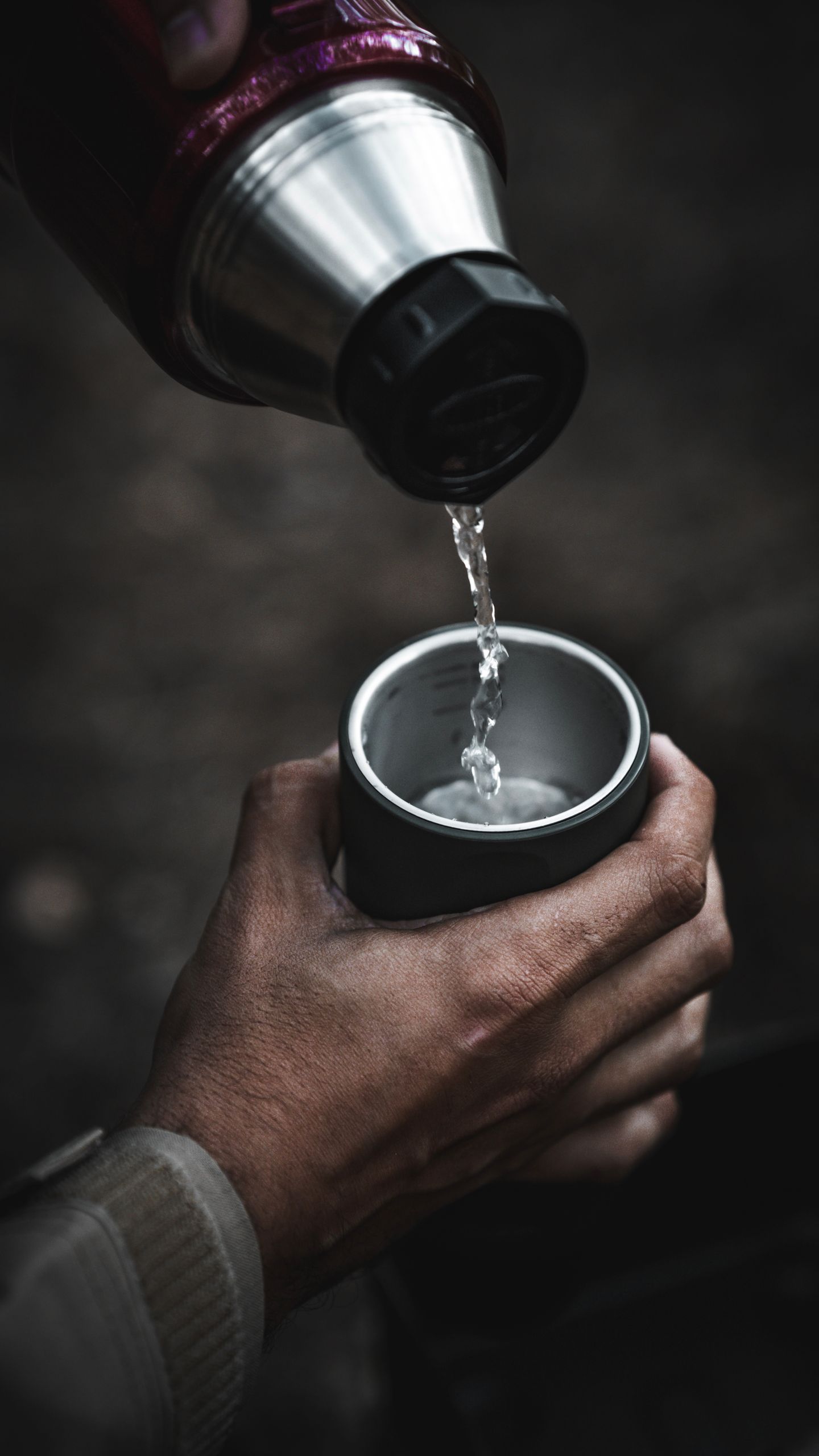 A close-up shot of water being poured from a thermos into a cup outdoors, capturing the essence of outdoor activities.