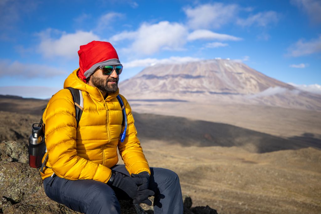 A man relaxing on Mount Kilimanjaro's slopes, dressed in warm outdoor clothing.
