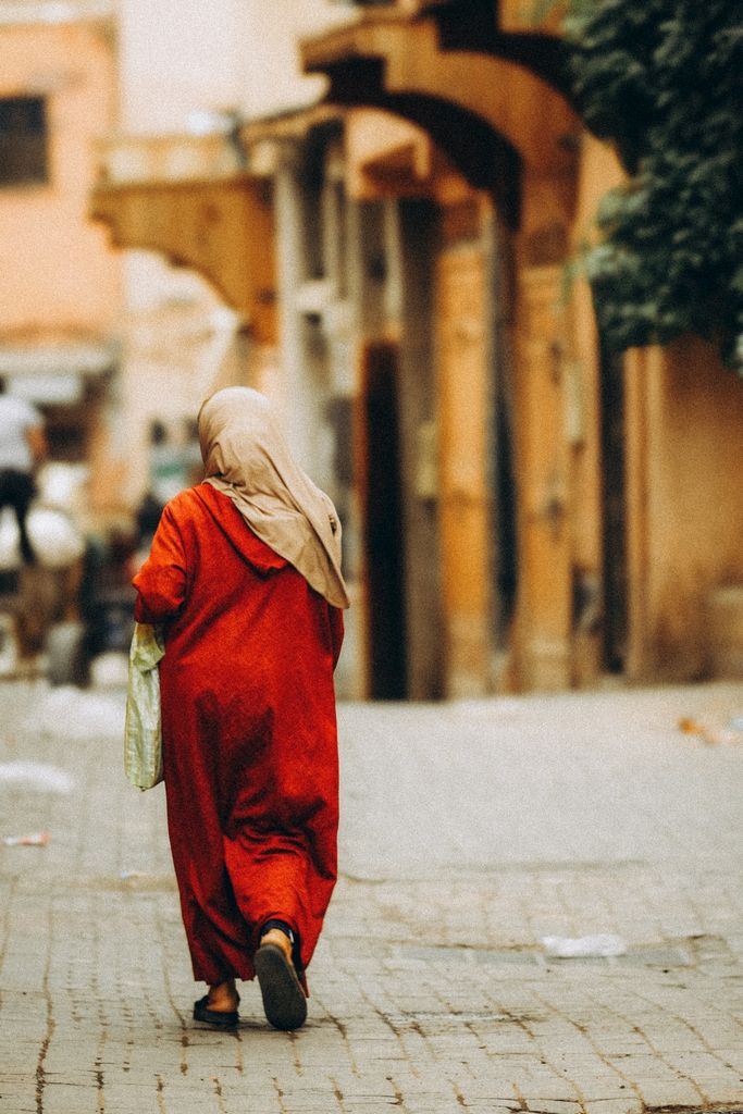 A woman in a red traditional dress walks down a vibrant Marrakech street.