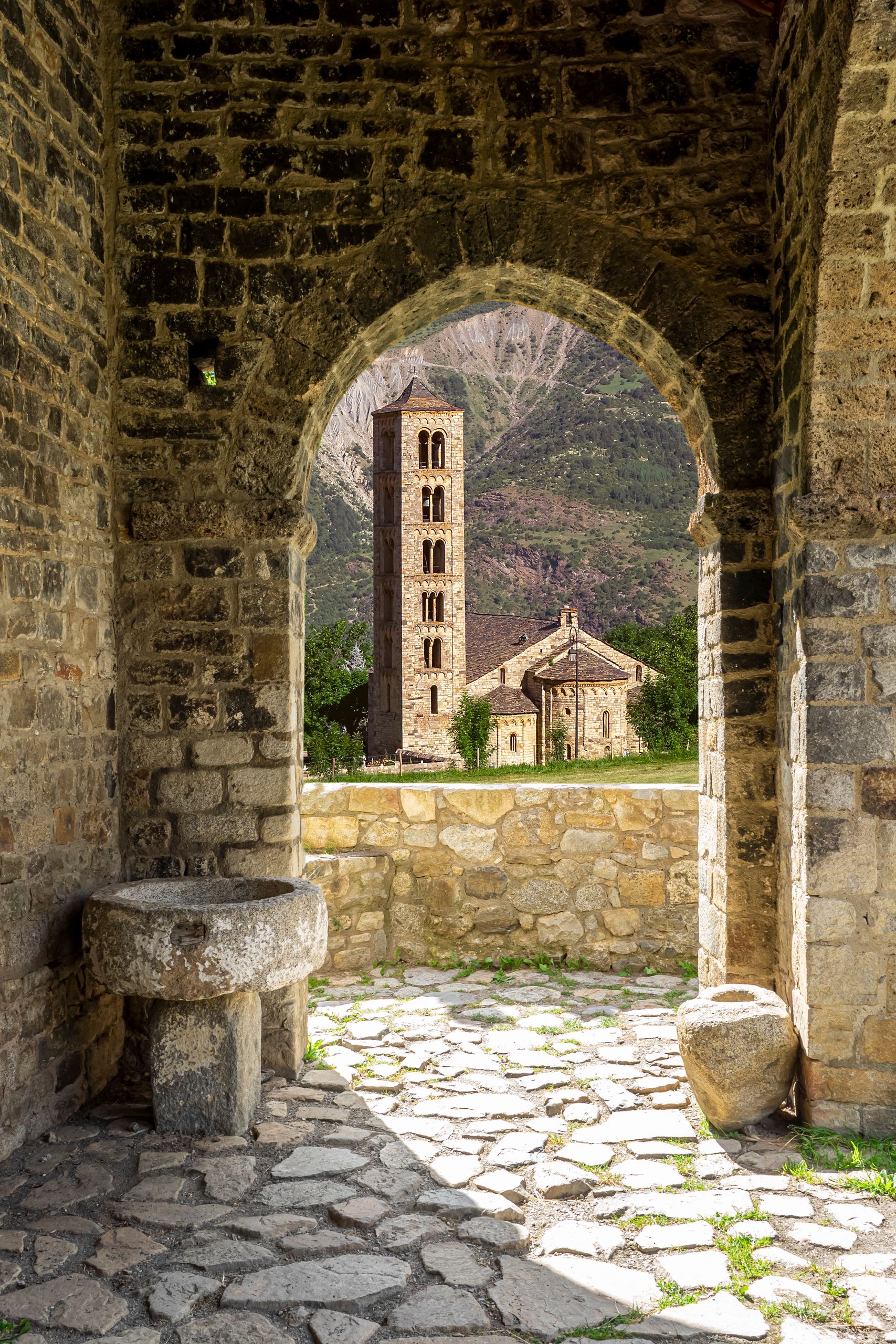 Beautiful view of a Romanesque church and bell tower through stone archway in Bohí, Spain.