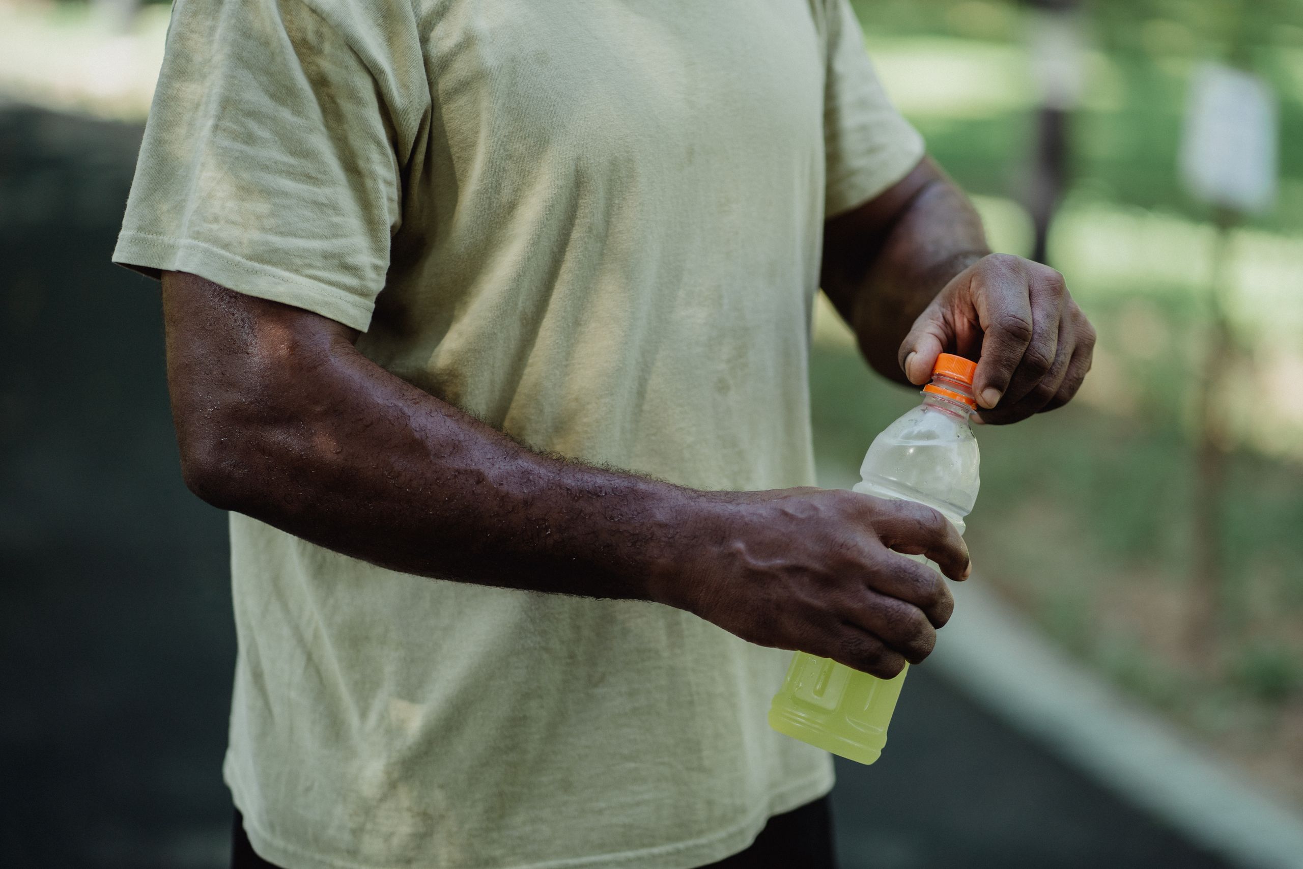 Close-up of a person opening a bottle of sports drink in a park setting.