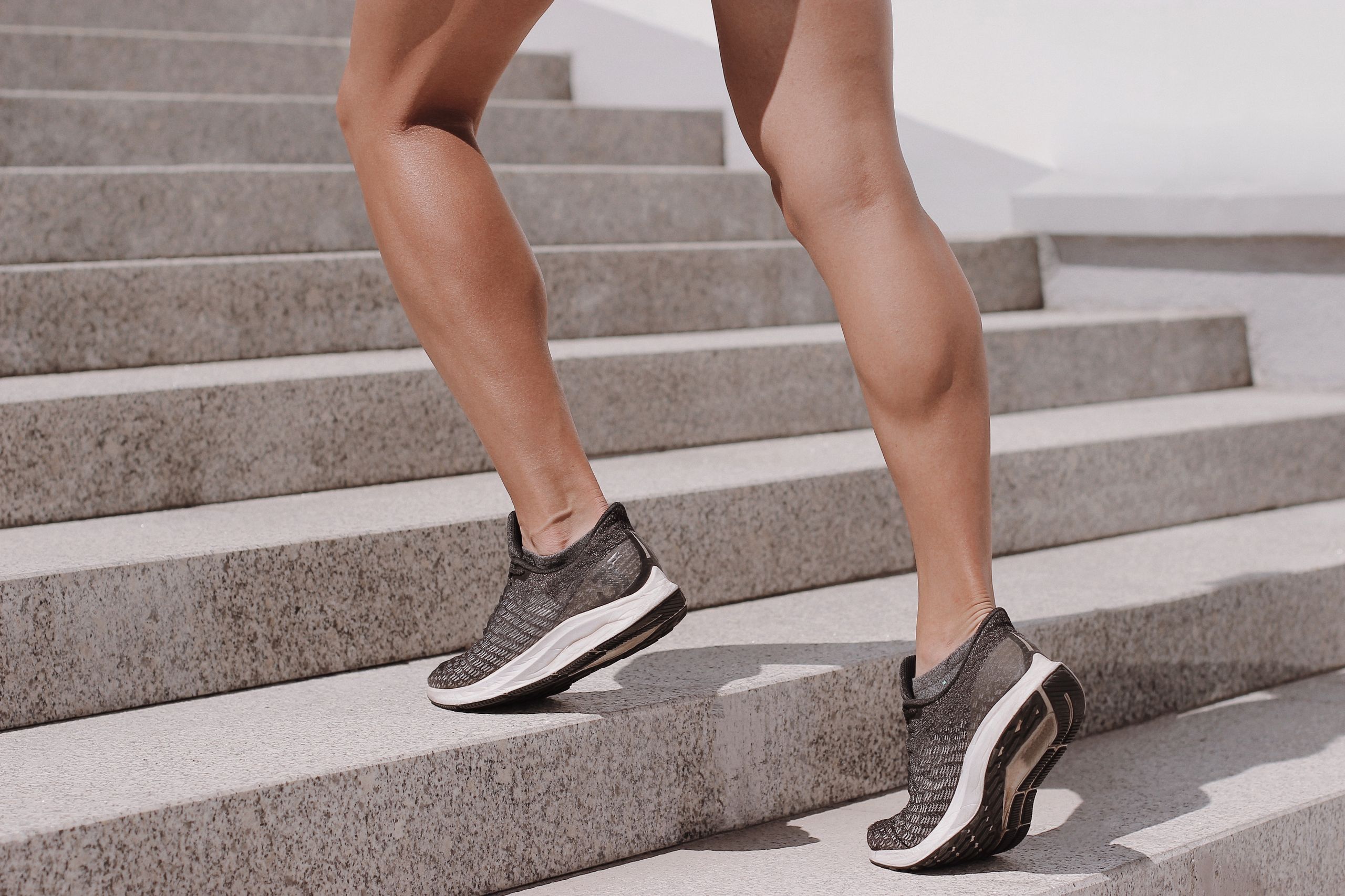 Close-up of an athlete in sneakers climbing outdoor stairs, showcasing toned muscles.
