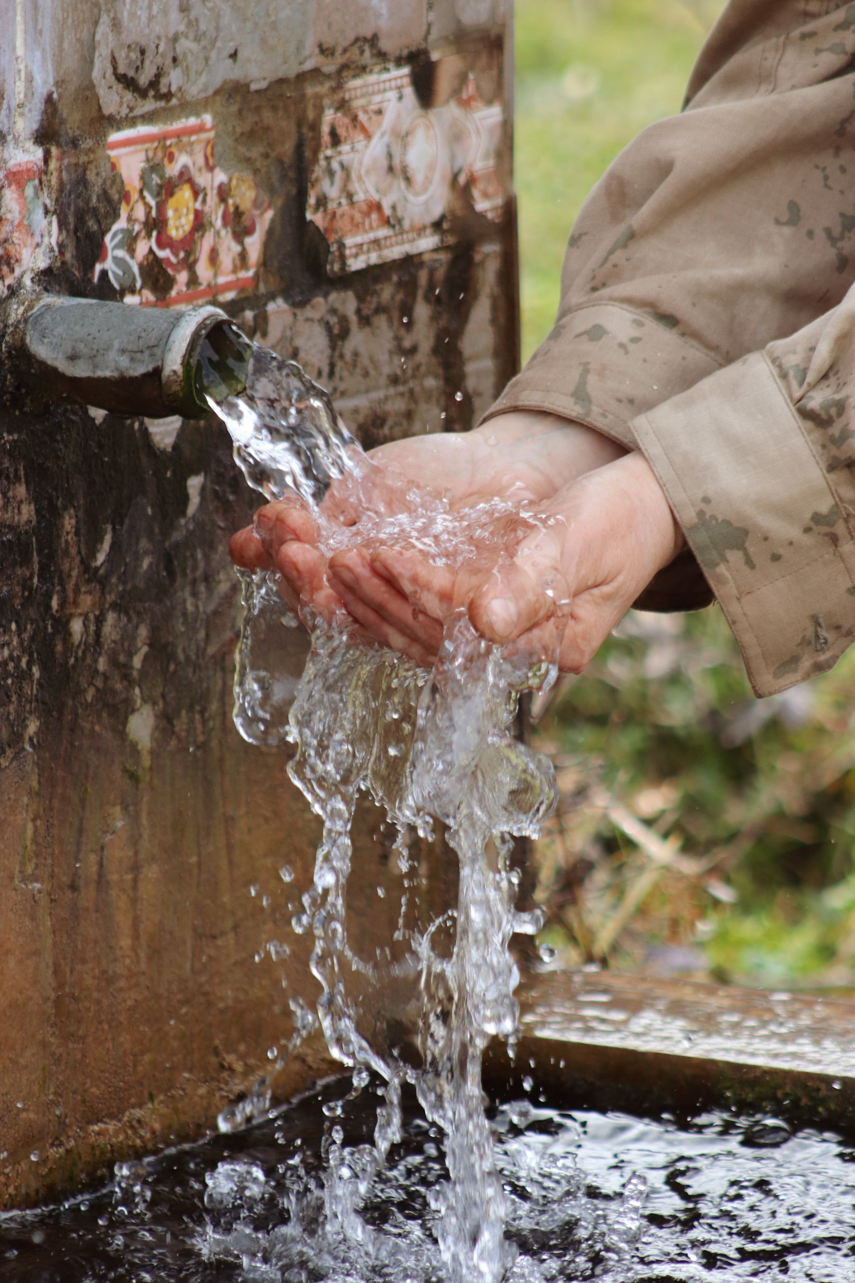 Close-up view of hands washing under flowing water outdoors, symbolizing hygiene and freshness.