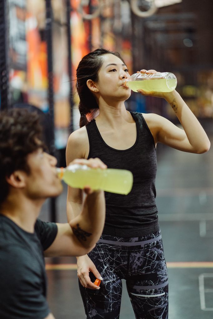 East Asian couple in activewear drinking energy drinks in a gym setting.