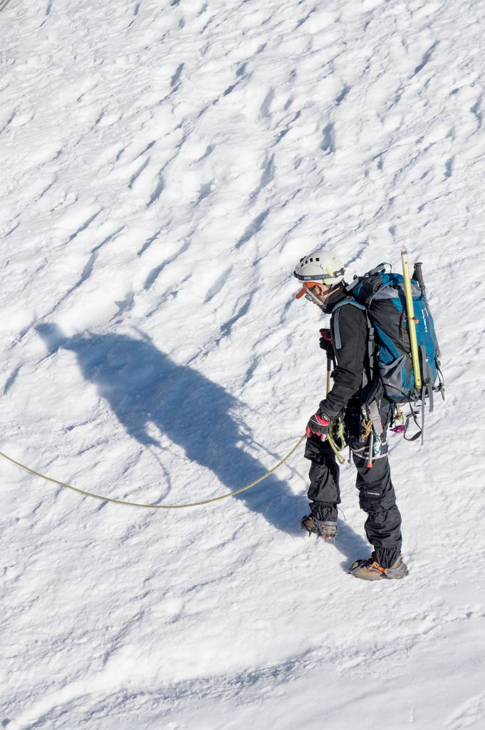 Experienced climber in sportswear and helmet ascends snow-covered mountain slope.