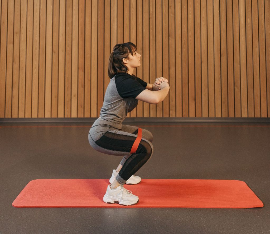 Female performing squats with a resistance band indoors on a mat, side view.