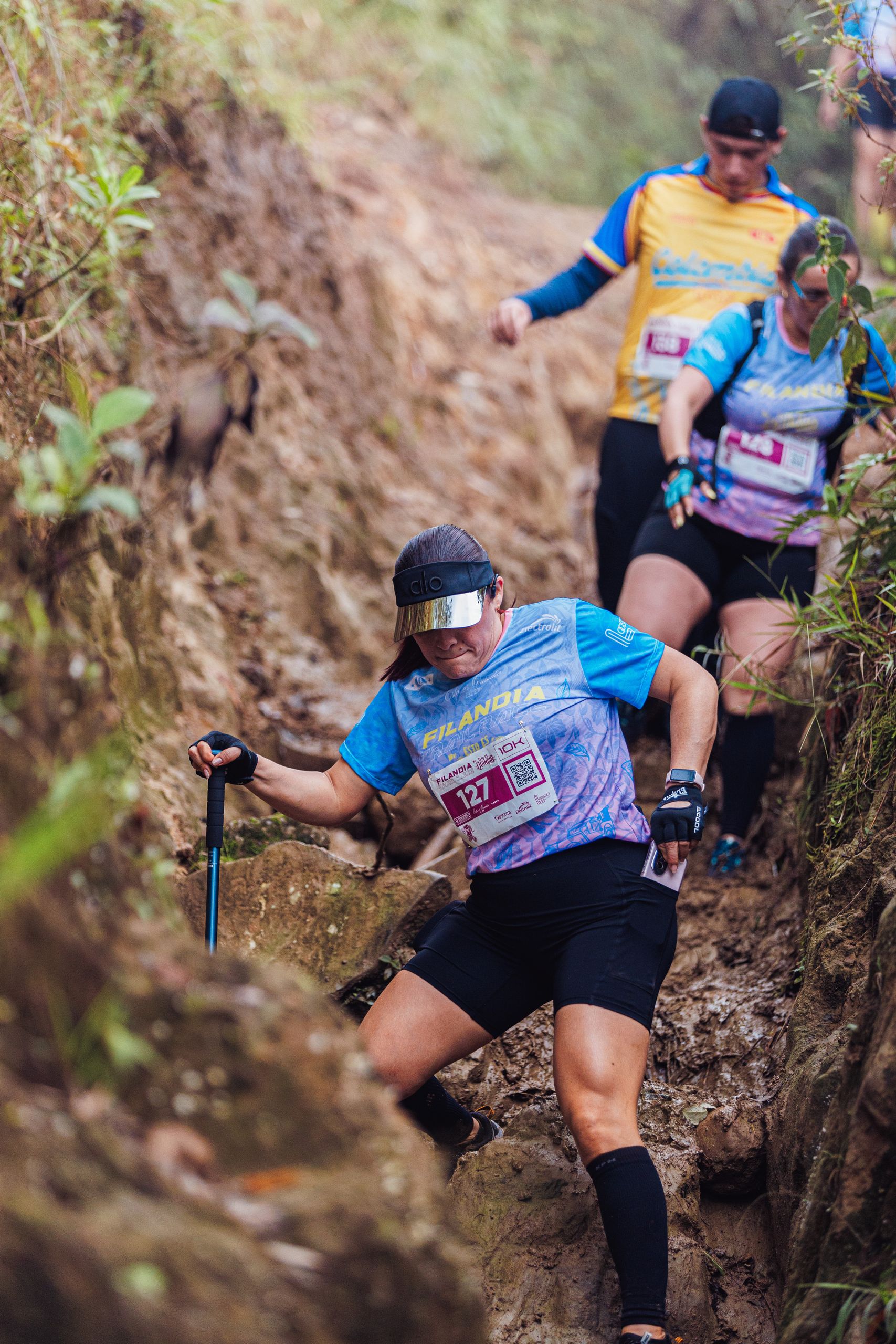 Group of trail runners carefully descending a narrow, muddy path during a forest race event.