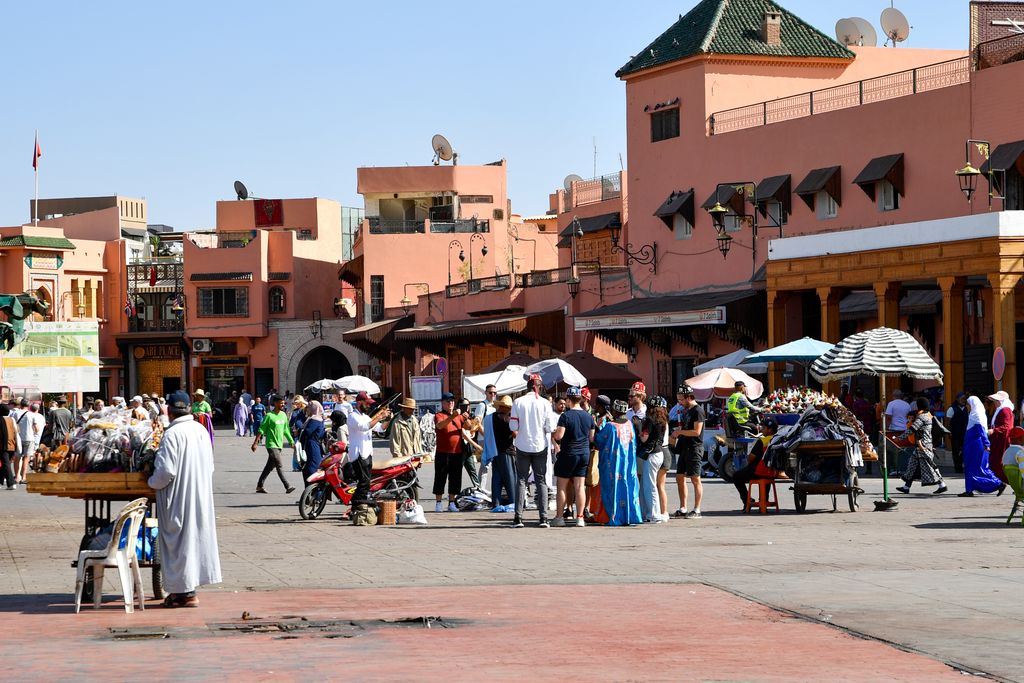 Lively market scene in Marrakesh with people shopping in Jemaa el-Fnaa square on a sunny day.