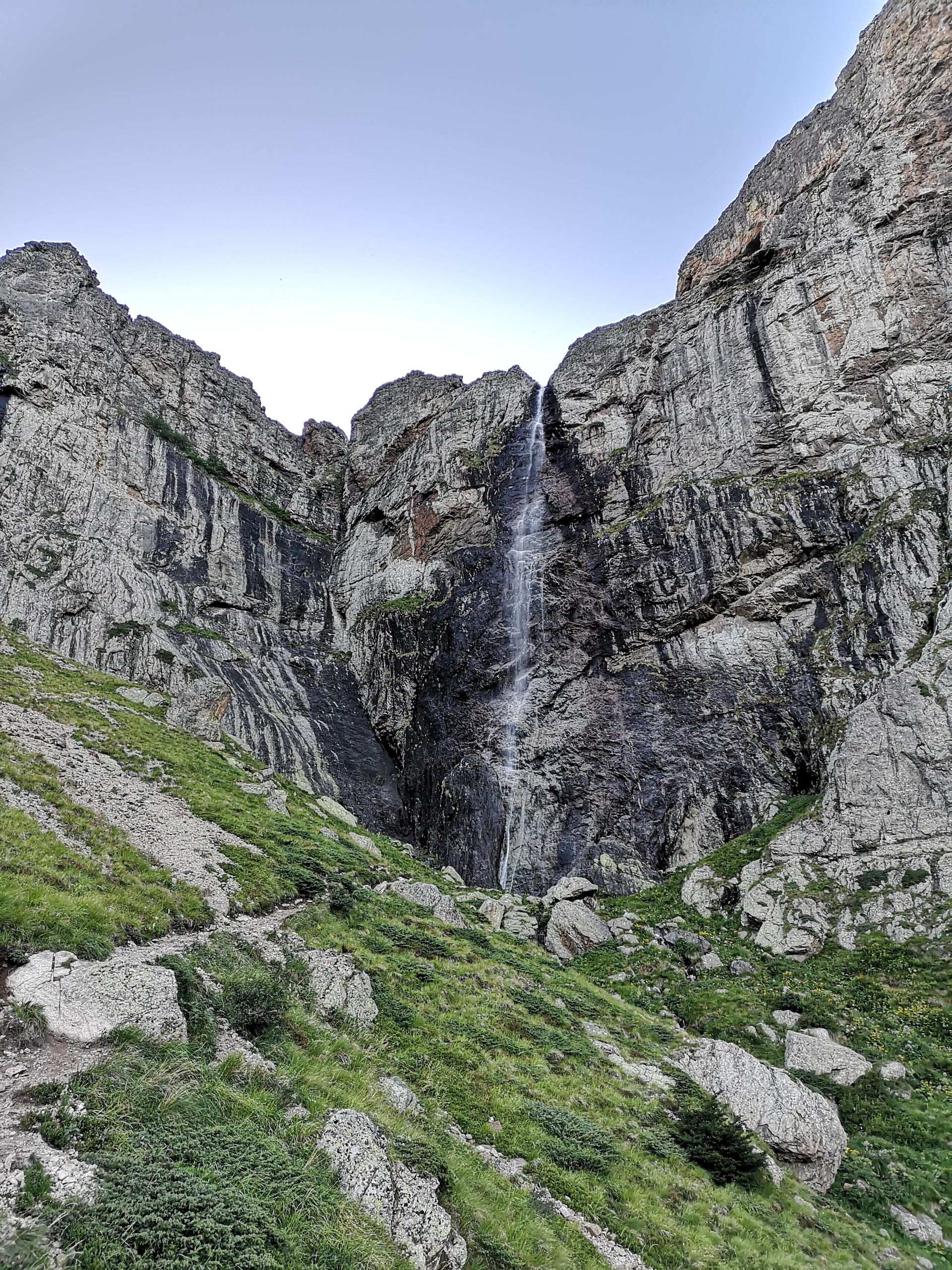 Majestic waterfall cascading down a rocky cliff in lush green surroundings.