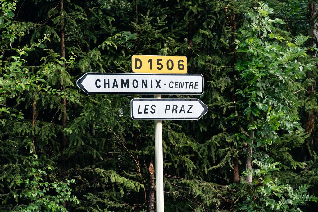 Road signs pointing to Chamonix Centre and Les Praz against a forest backdrop in France.