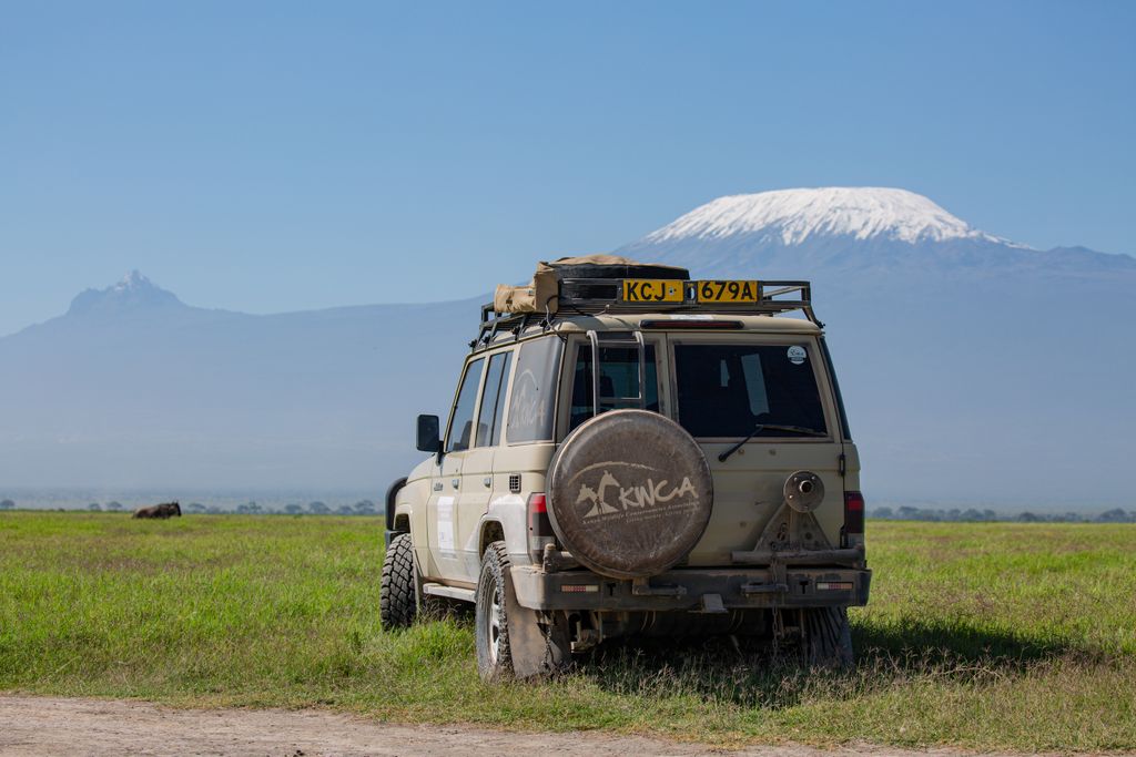 SUV parked on a grassy field with Mount Kilimanjaro in the background under a clear blue sky.