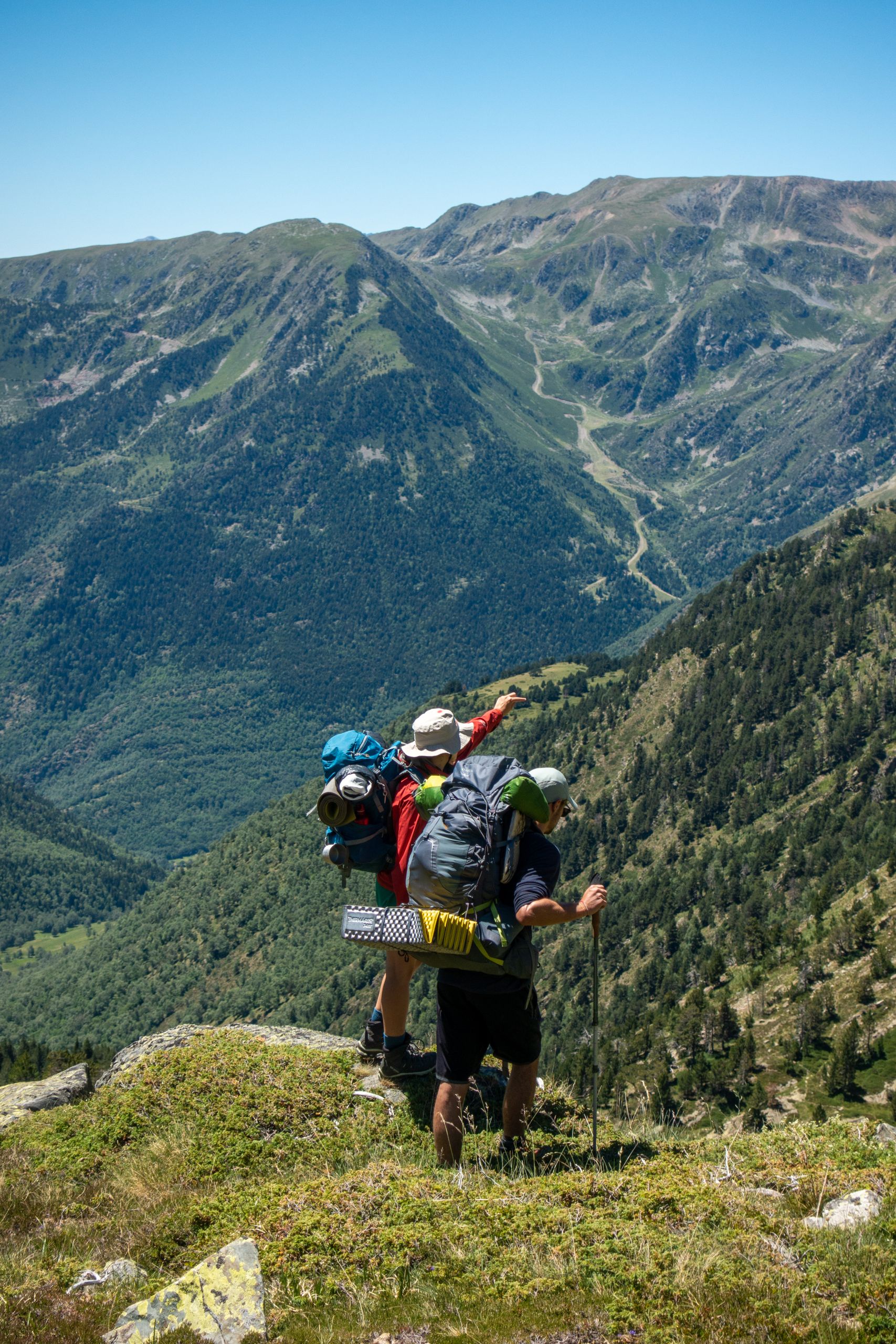 Two backpackers trekking in the mountains of Spain, enjoying a sunlit summer day.
