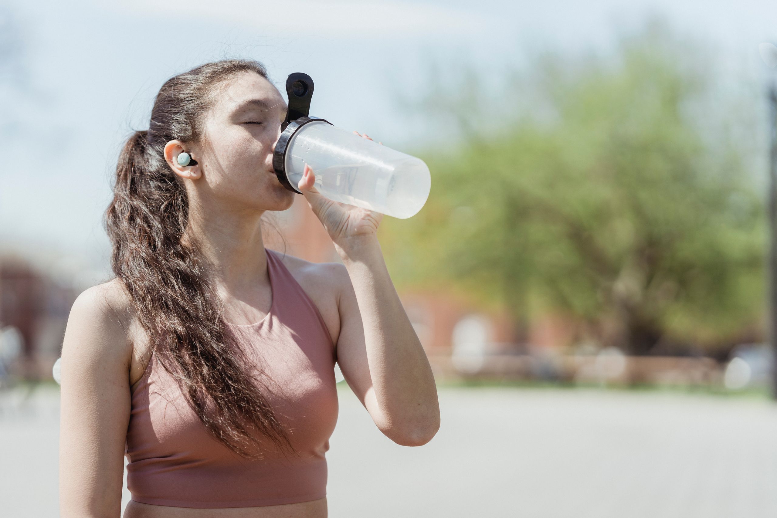 Young woman in sportswear drinks water outdoors, enjoying a sunny day.